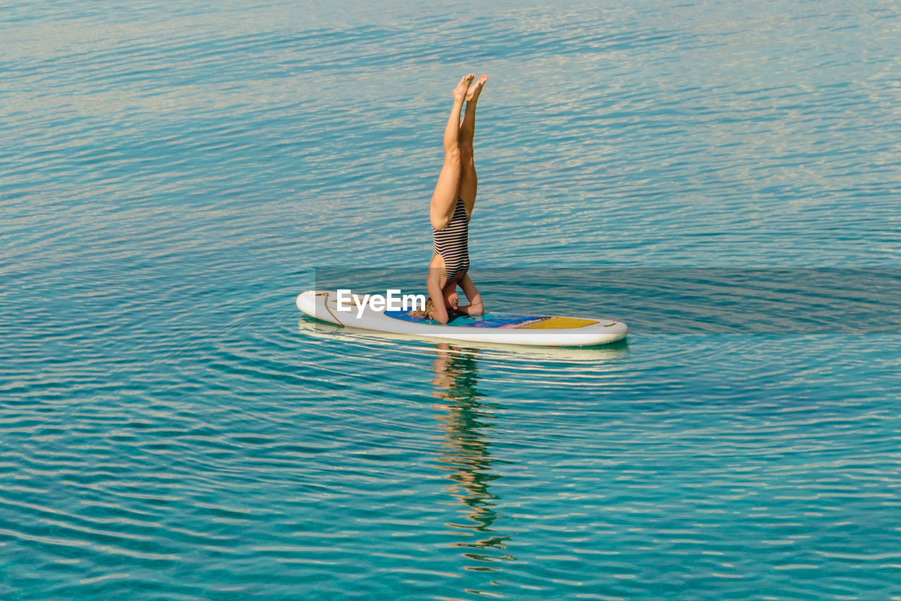 Full length of woman doing headstand on surfboard in sea