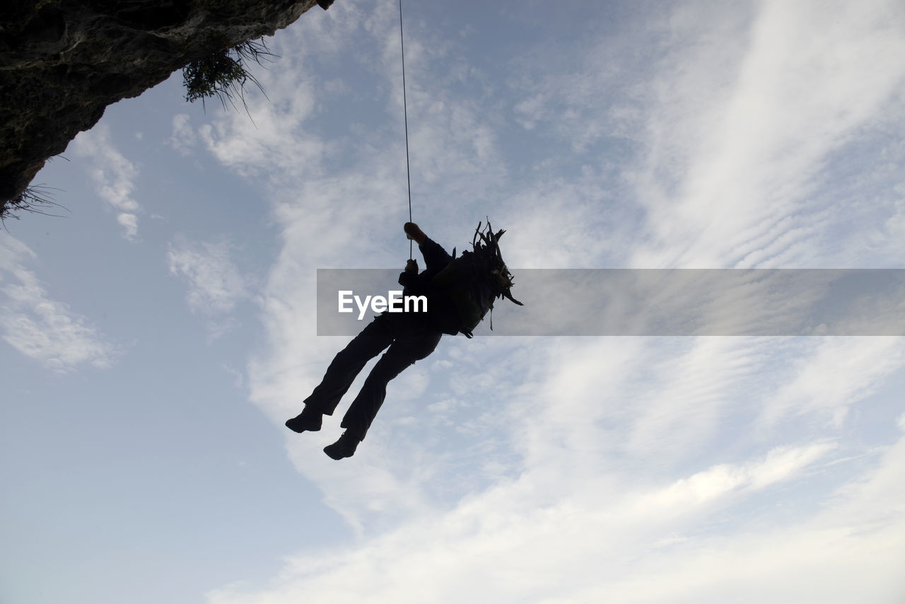 Low angle view of a man hangs to a rope