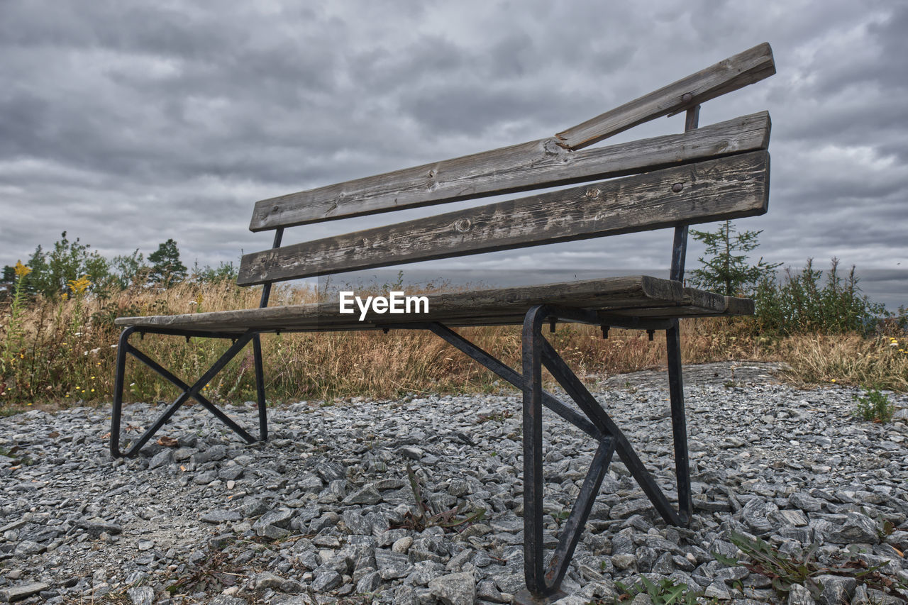 EMPTY BENCH IN FIELD AGAINST SKY