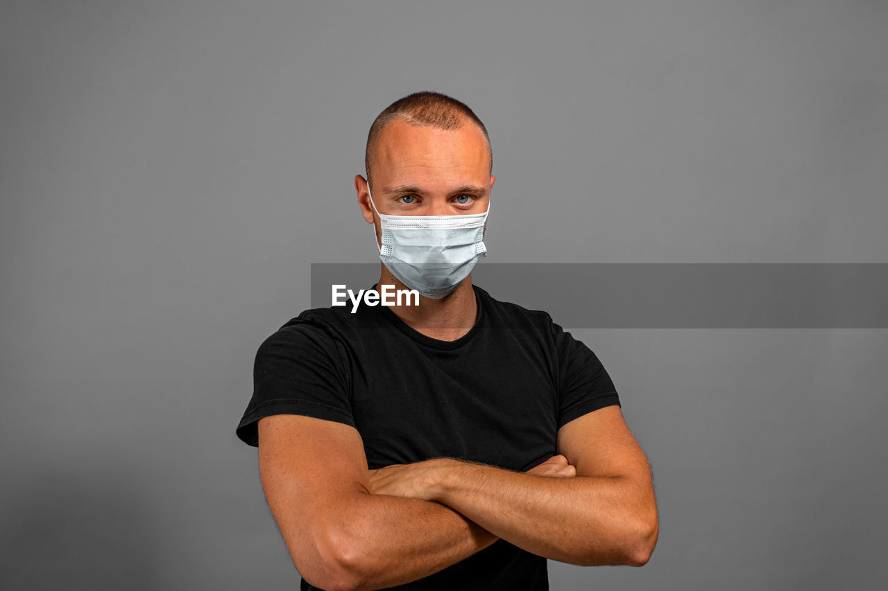 PORTRAIT OF YOUNG MAN WEARING MASK AGAINST GRAY BACKGROUND