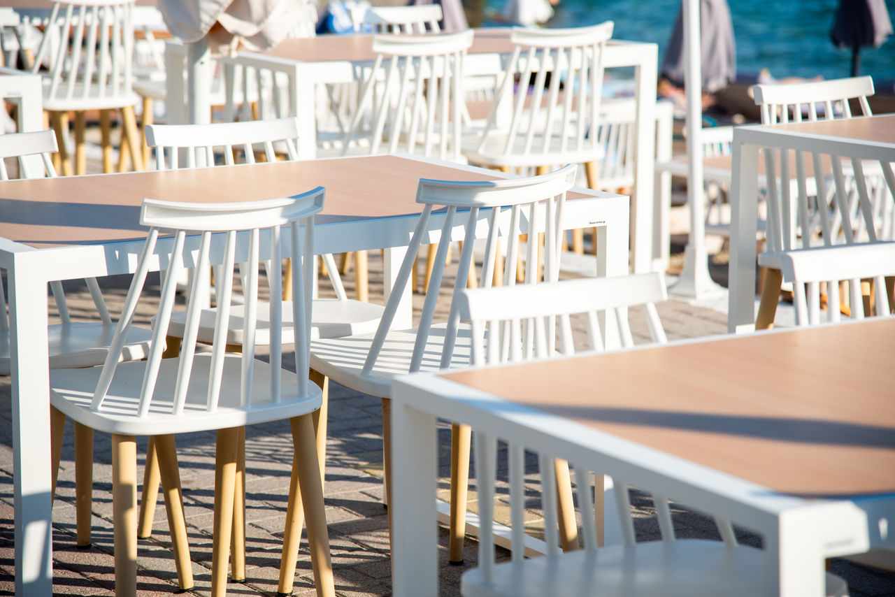 chair, seat, table, restaurant, cafe, business, empty, furniture, room, relaxation, wood, in a row, architecture, water, no people, food and drink, nature, sunlight, setting, absence, meal, travel destinations, day, arrangement, sidewalk cafe, luxury, travel, outdoors, dining table, white
