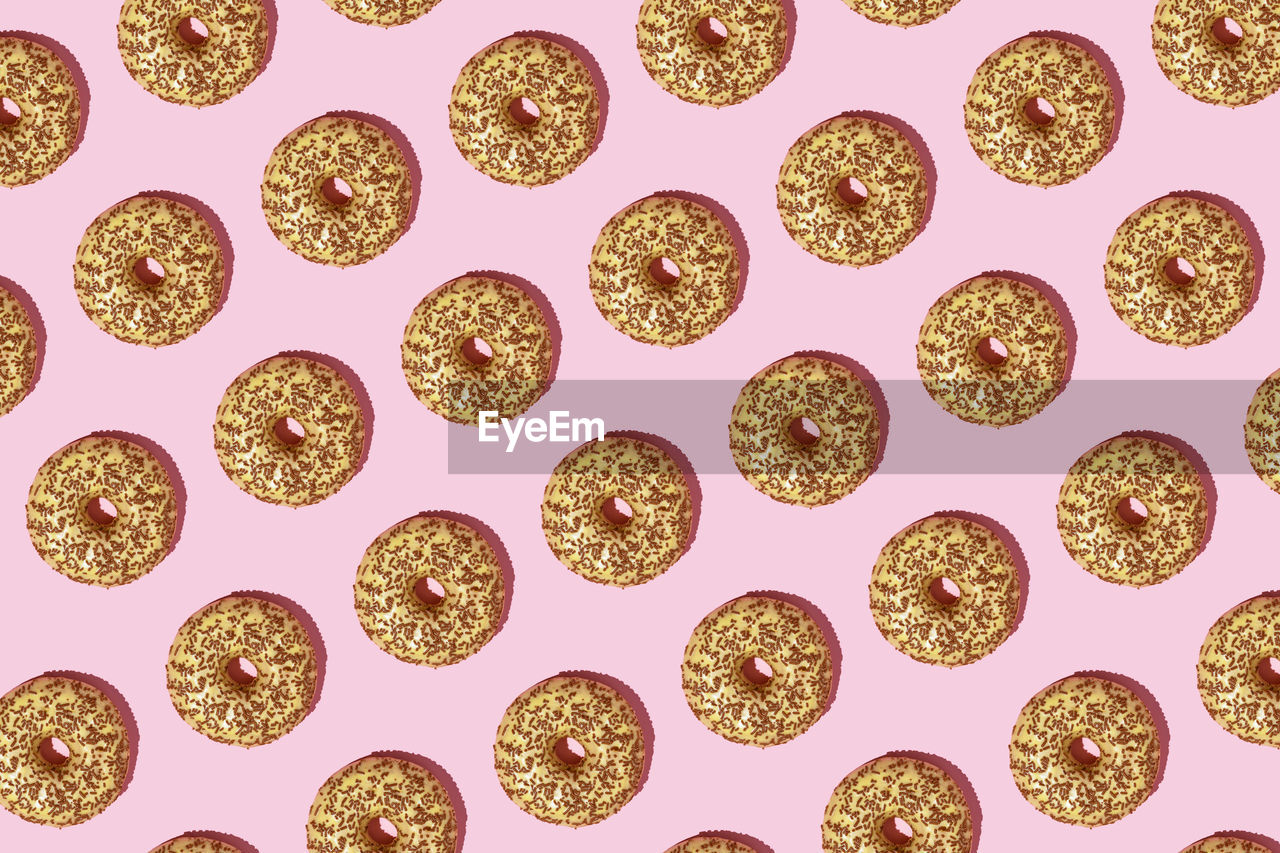Seamless pattern of donuts with chocolate over it against pink pastel background.