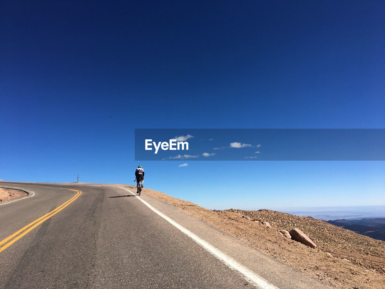Rear view of man riding bicycle on road against clear blue sky