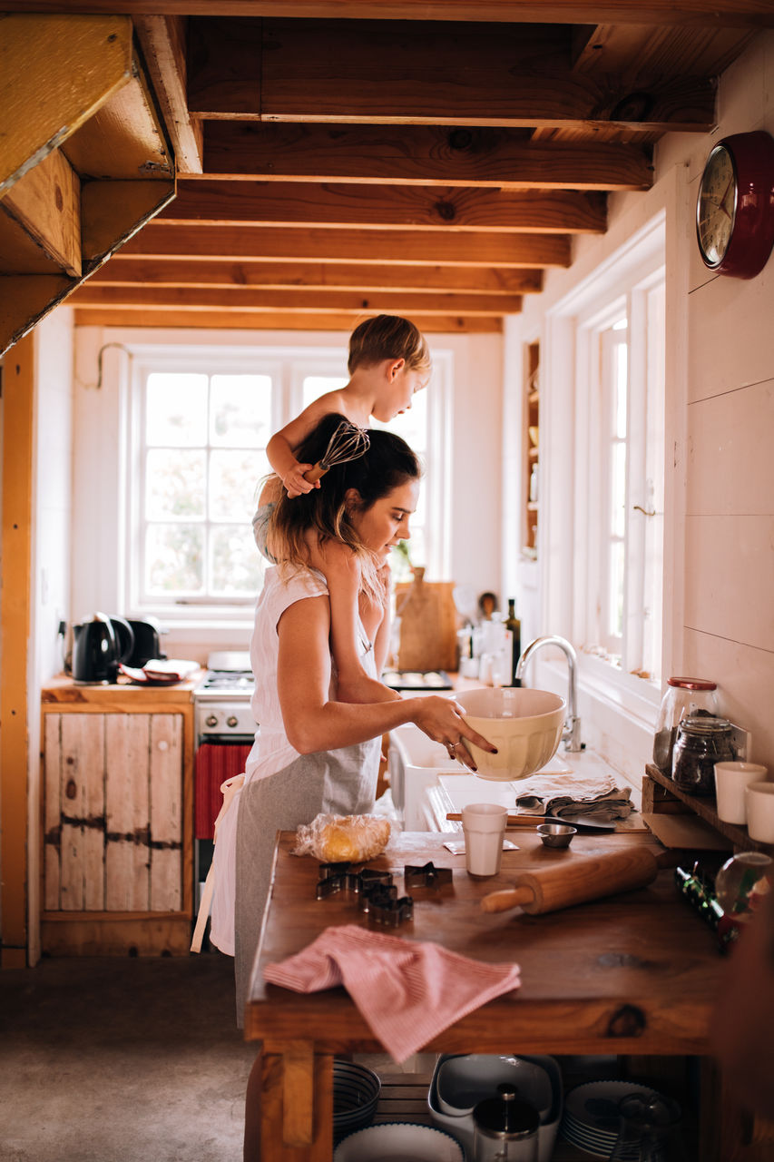 Mother carrying cute son on shoulders while standing in kitchen