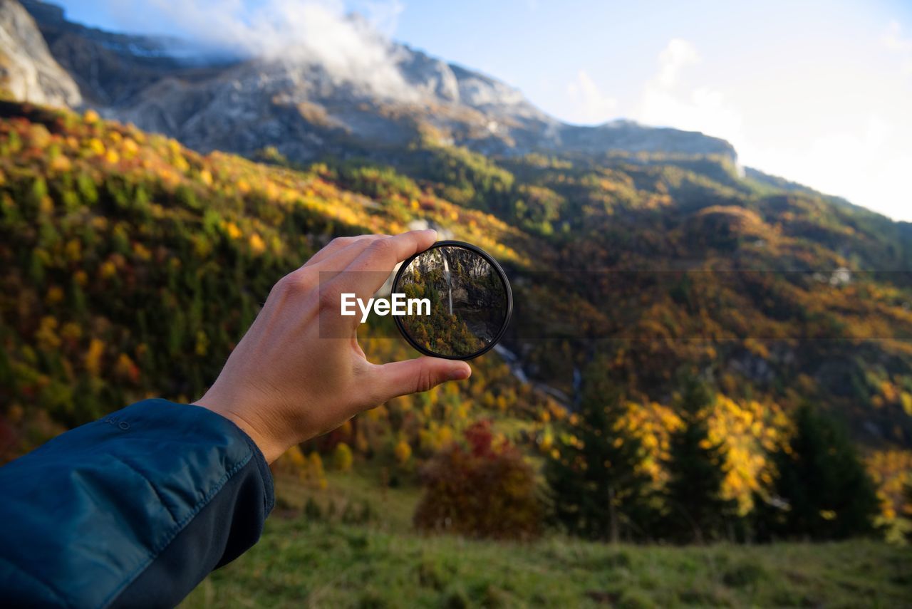 Close-up of hand holding lens against mountains