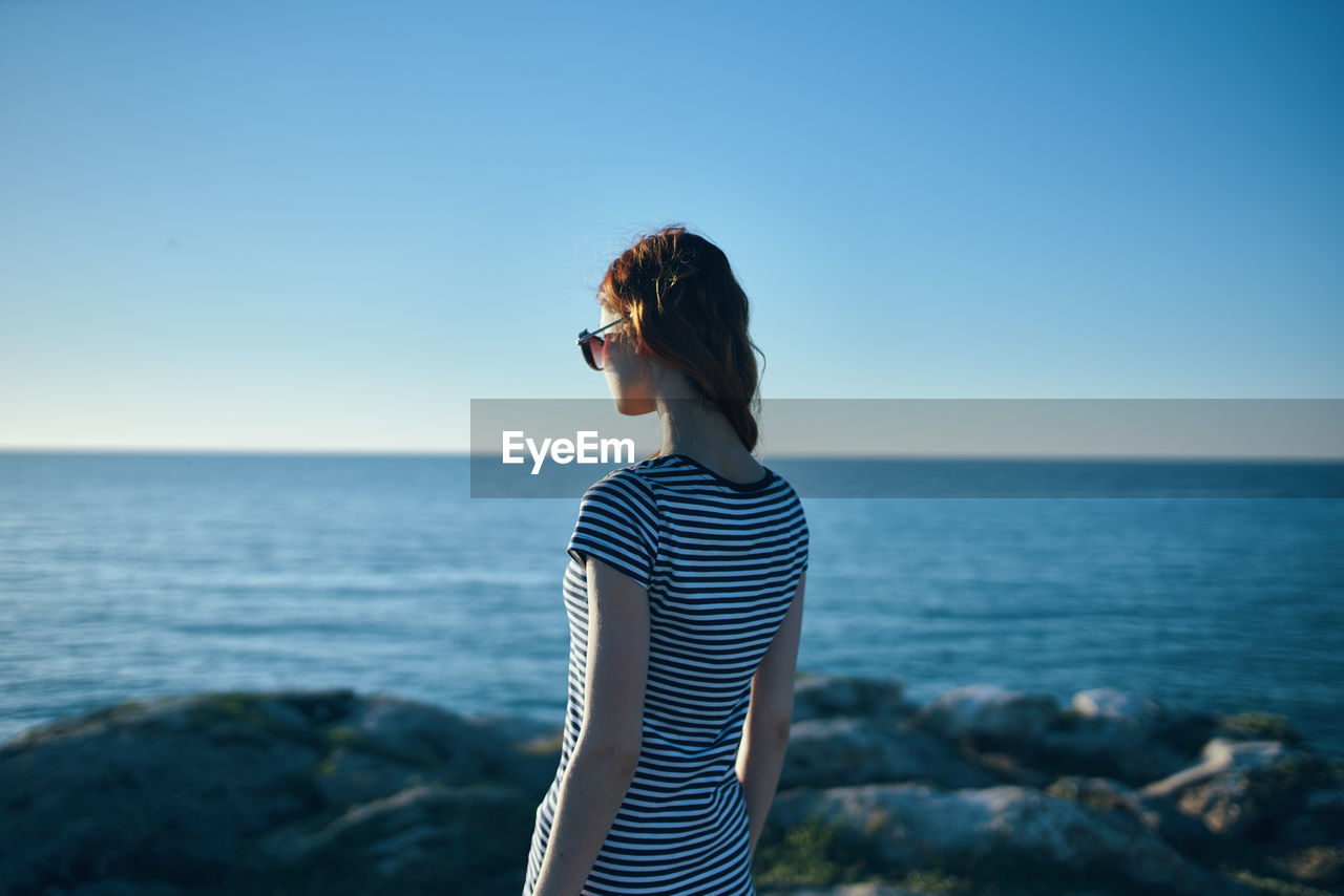 Young woman looking at sea against clear sky