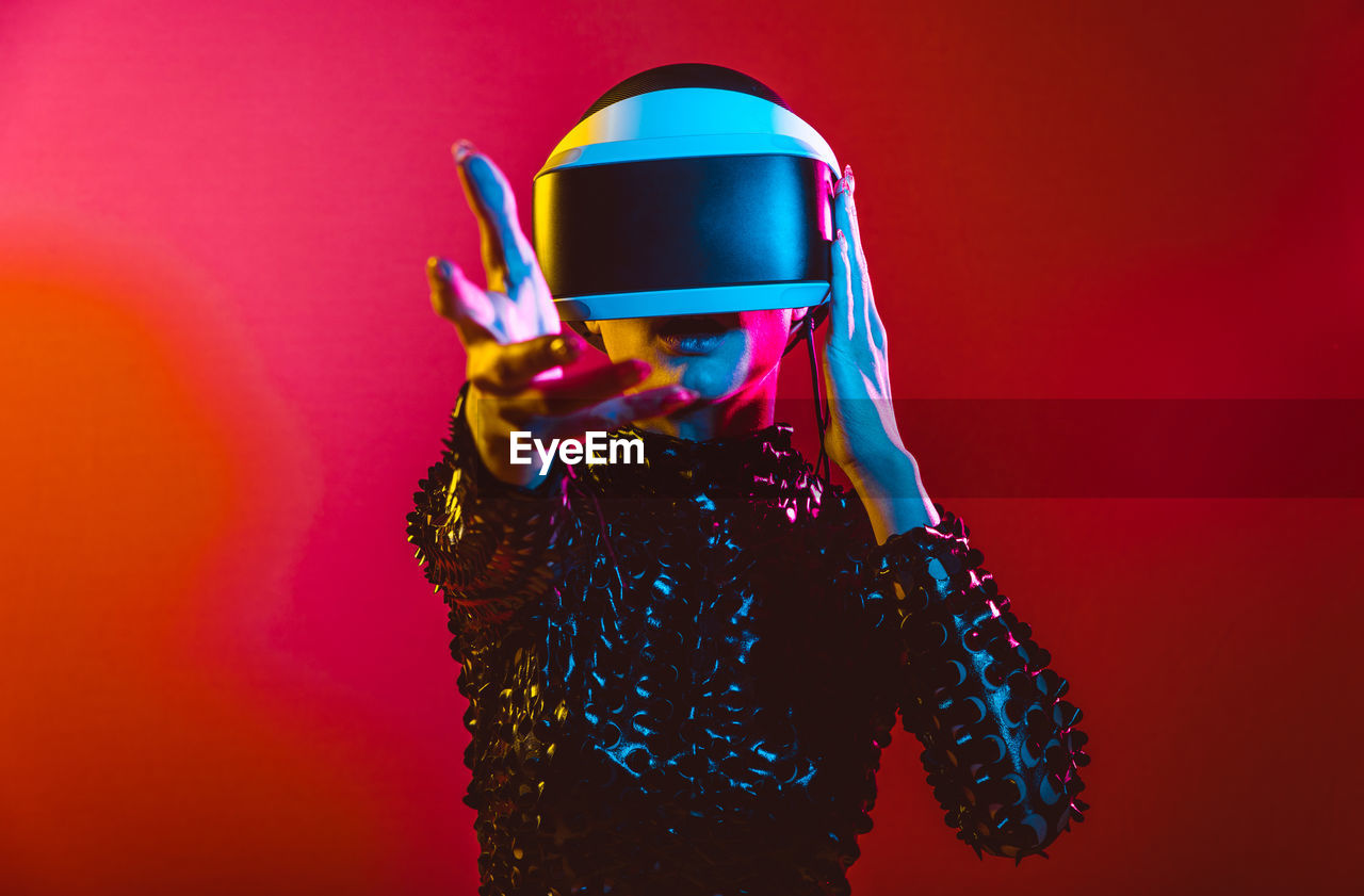 Young woman with shaved head wearing virtual reality glasses against pink background