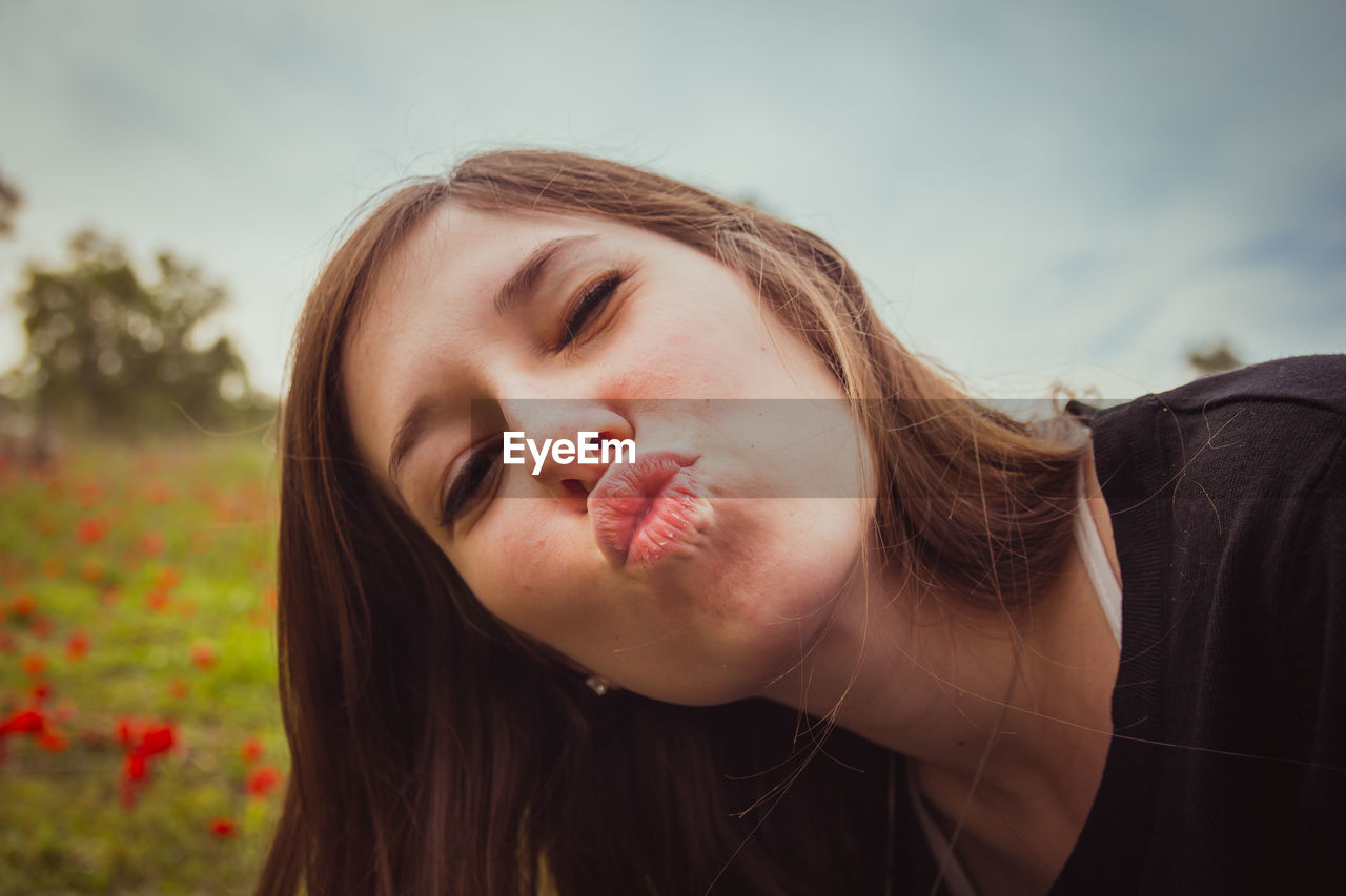 Close-up portrait of beautiful young woman puckering against sky