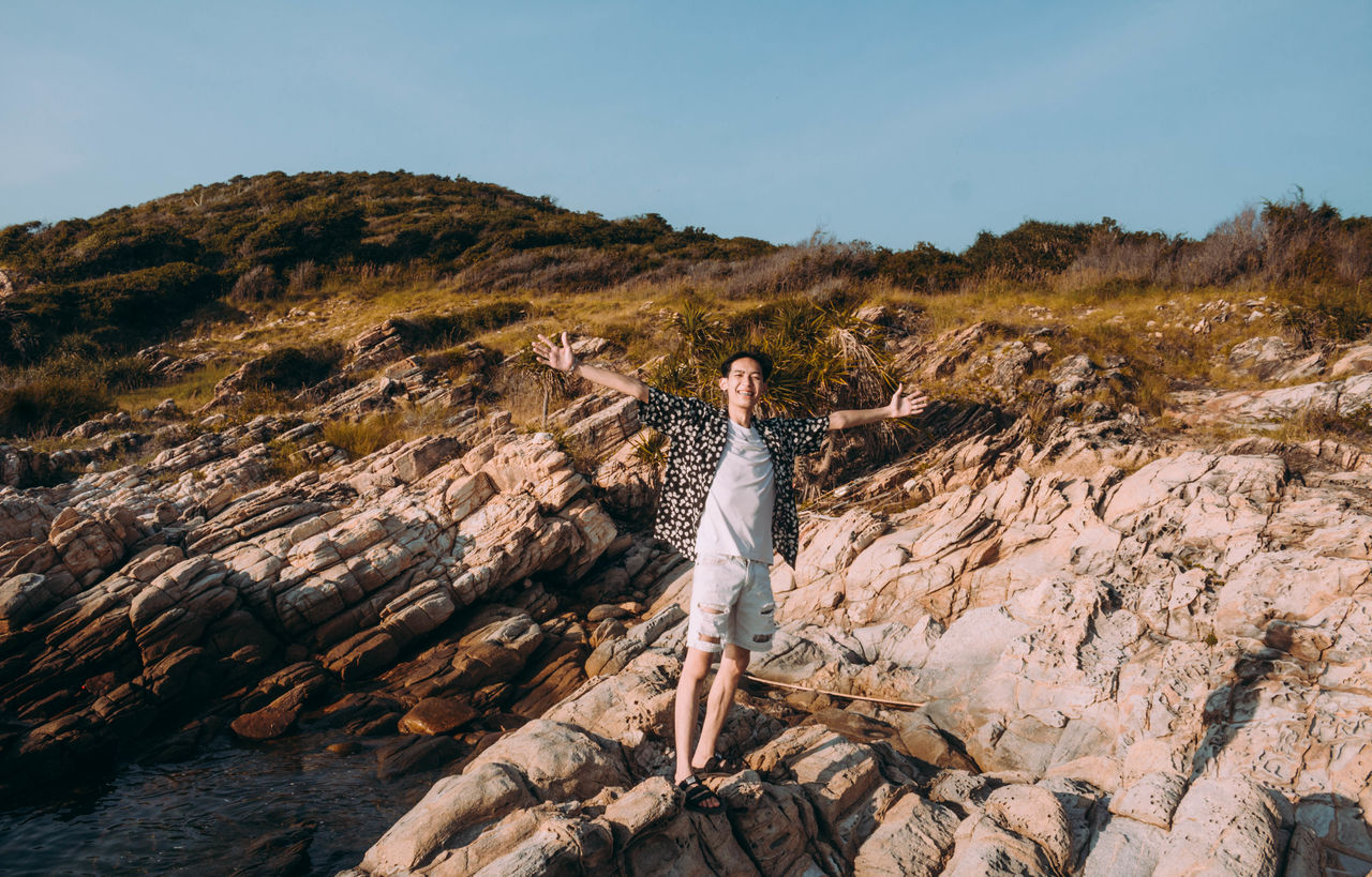 Full length of man with arms outstretched standing on rock