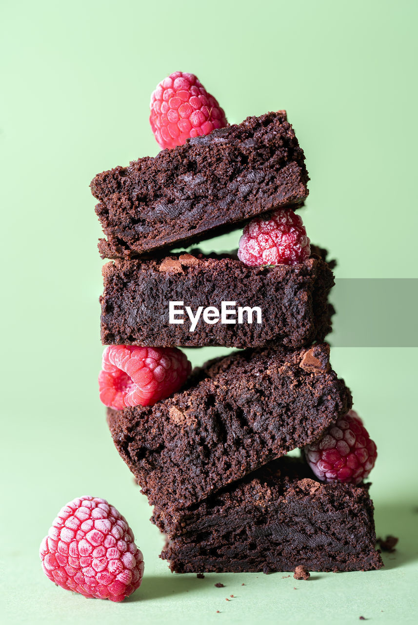 Chocolate brownies and raspberries fruits in a stack on a green mint background. chocolate dessert.