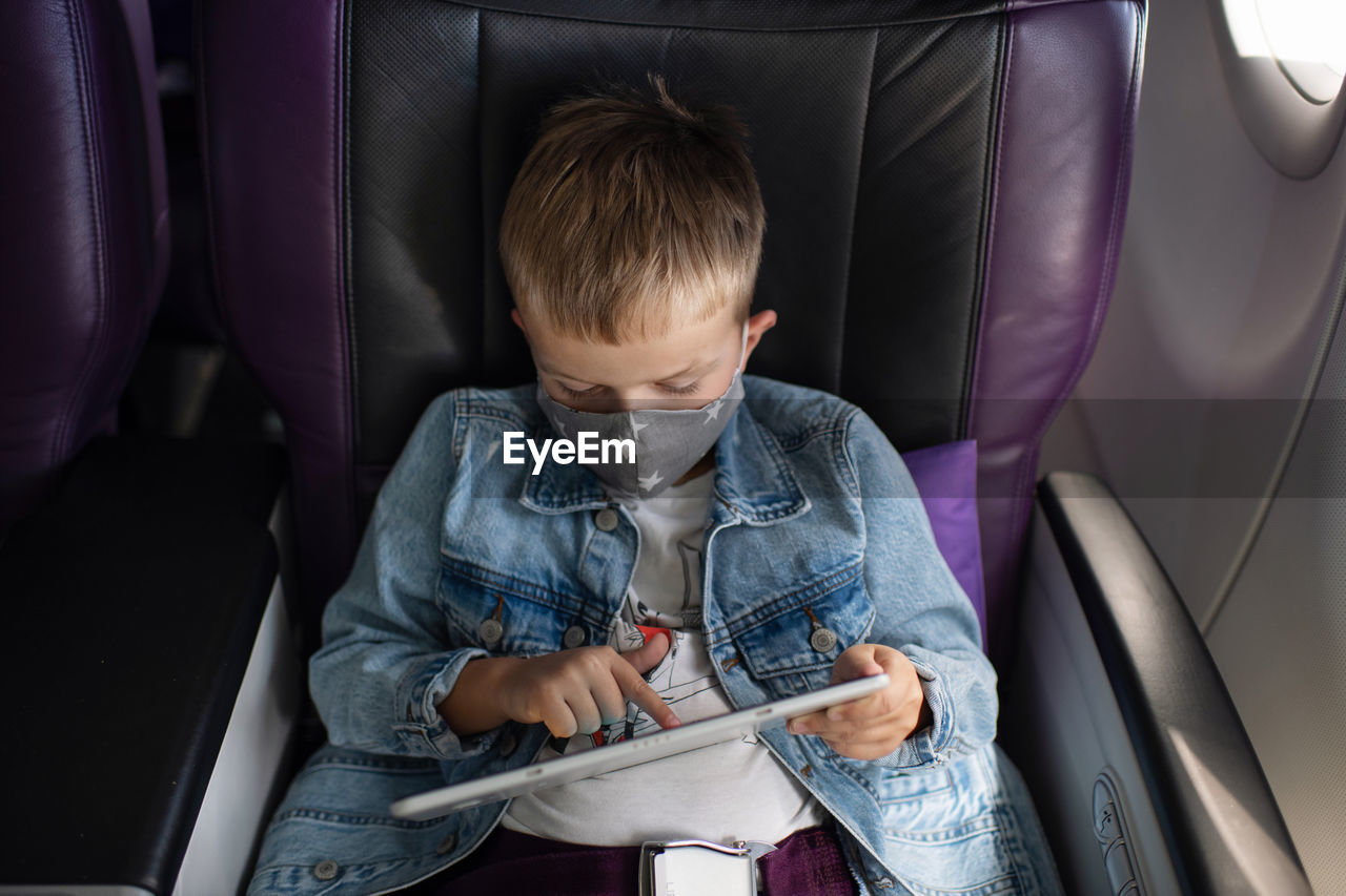 High angle view of boy wearing flu mask using digital tablet in airplane