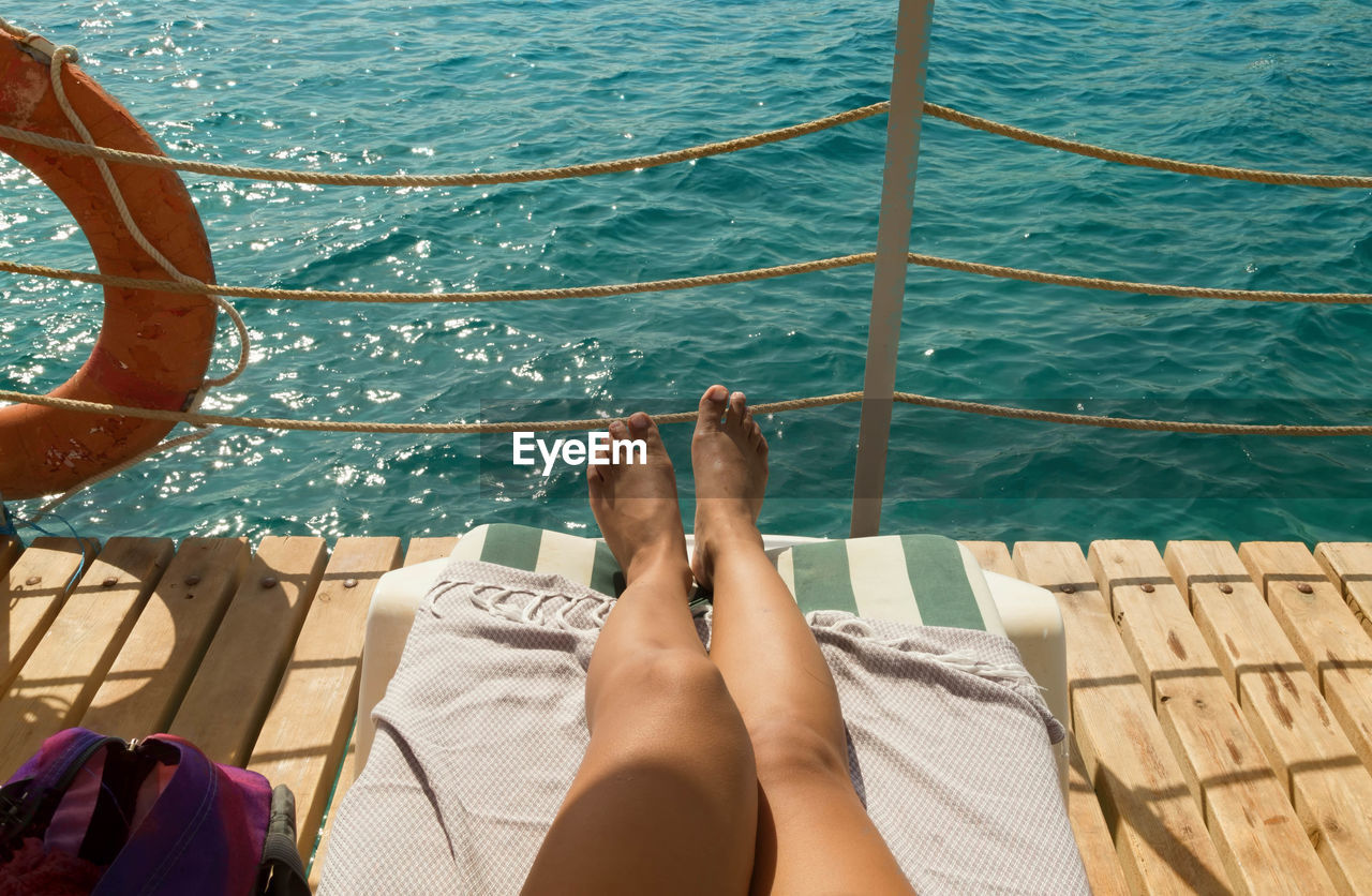 Low section of woman sunbathing on pier over sea