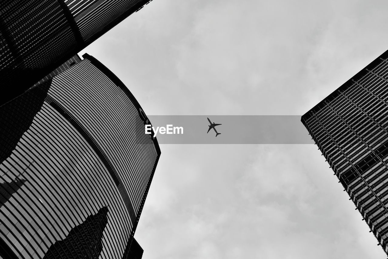 Low angle view of airplane flying over buildings against sky