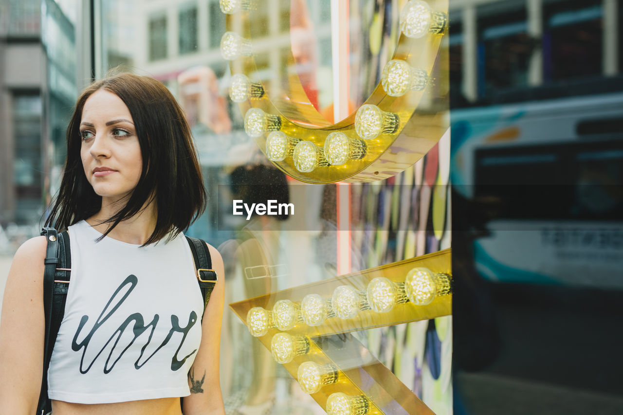 Woman standing by glass wall in city