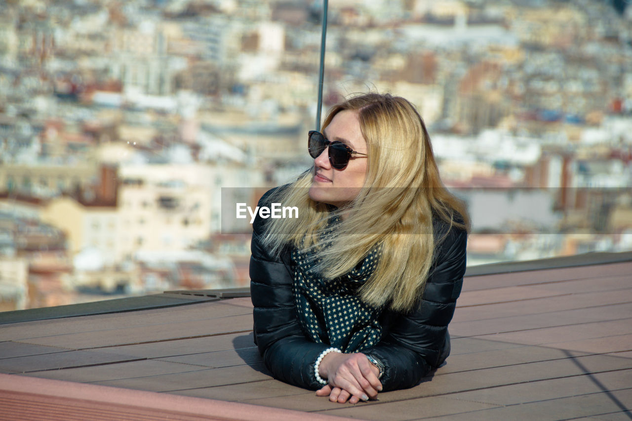 Young woman looking away while lying against cityscape