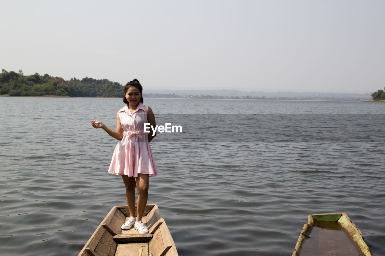 Portrait of young woman standing on boat by sea against clear sky