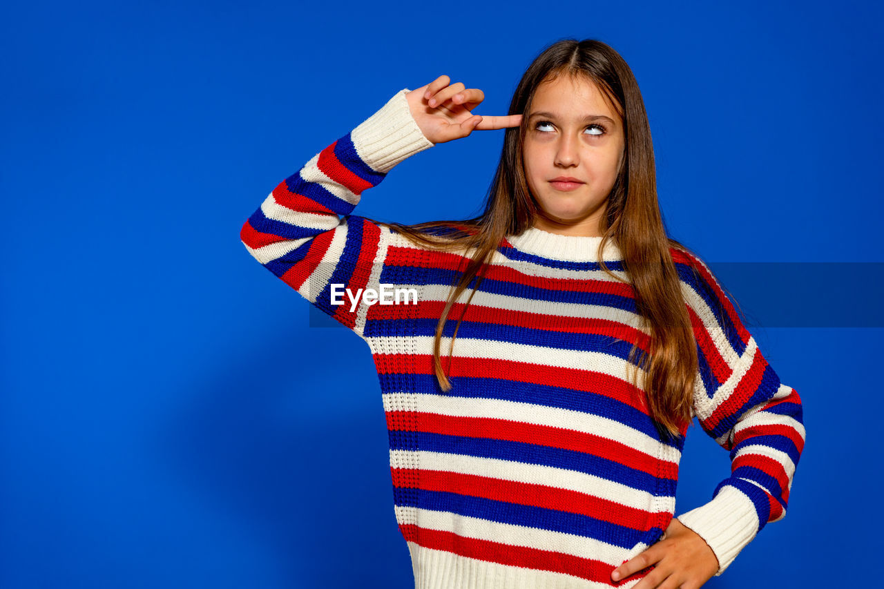 blue, striped, one person, studio shot, portrait, colored background, young adult, looking at camera, women, waist up, blue background, adult, clothing, emotion, standing, hairstyle, casual clothing, indoors, child, long hair, photo shoot, brown hair, copy space, arm, limb, sweater, hand, front view, human limb, happiness, looking, fashion, teenager, lifestyles, person