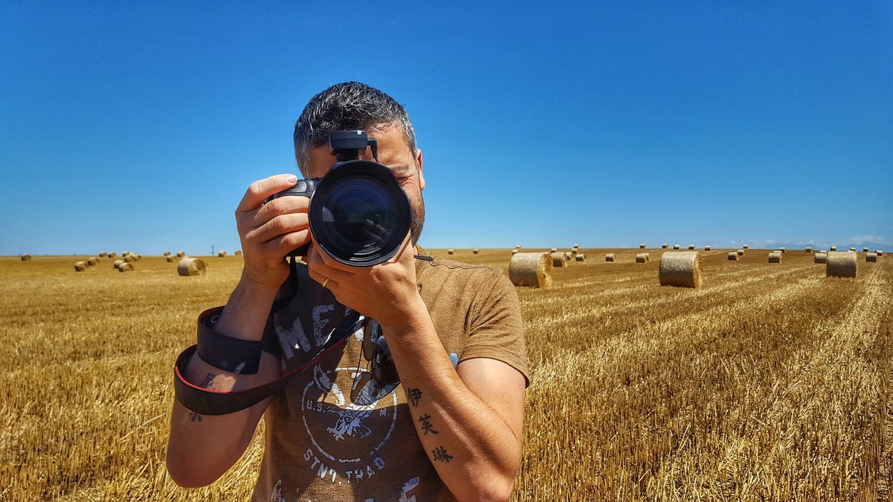 Man photographing through digital camera against hay bales on field