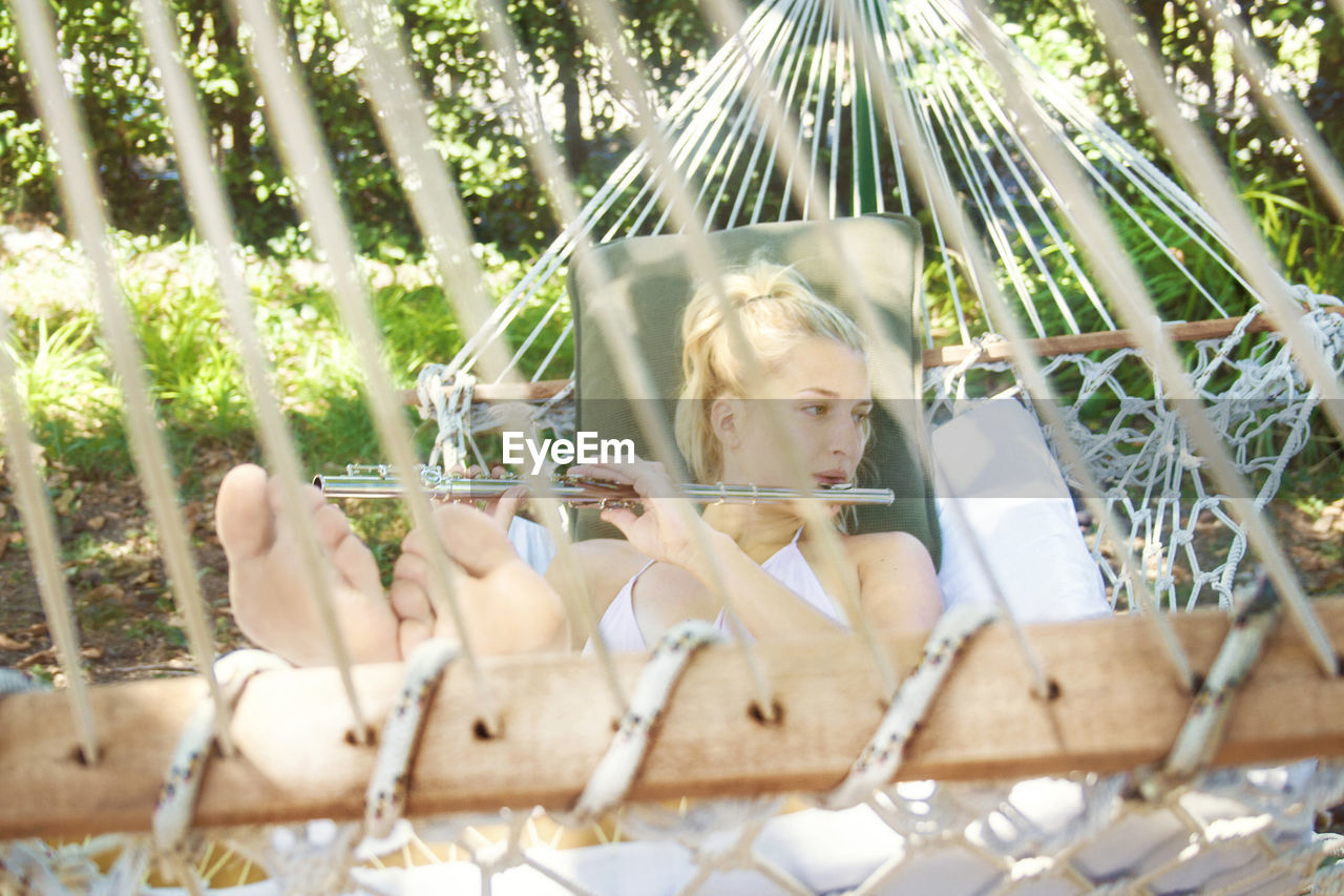 Beautiful young woman playing flute while lying on hammock