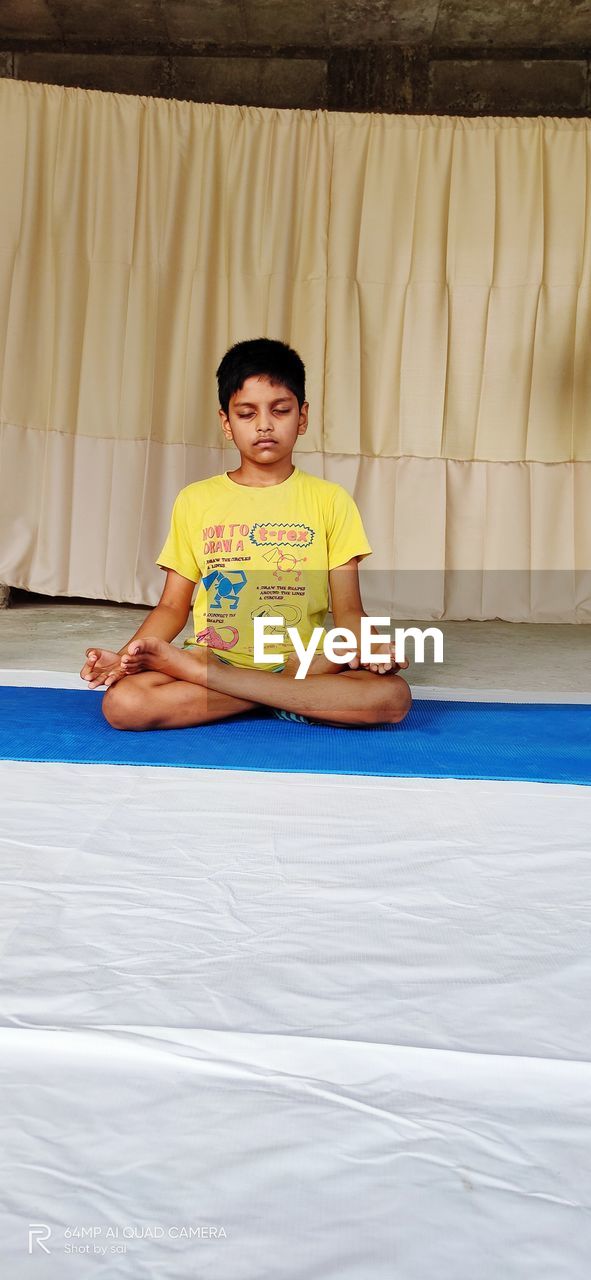 Portrait of a smiling boy sitting lotus pose on yoga mat