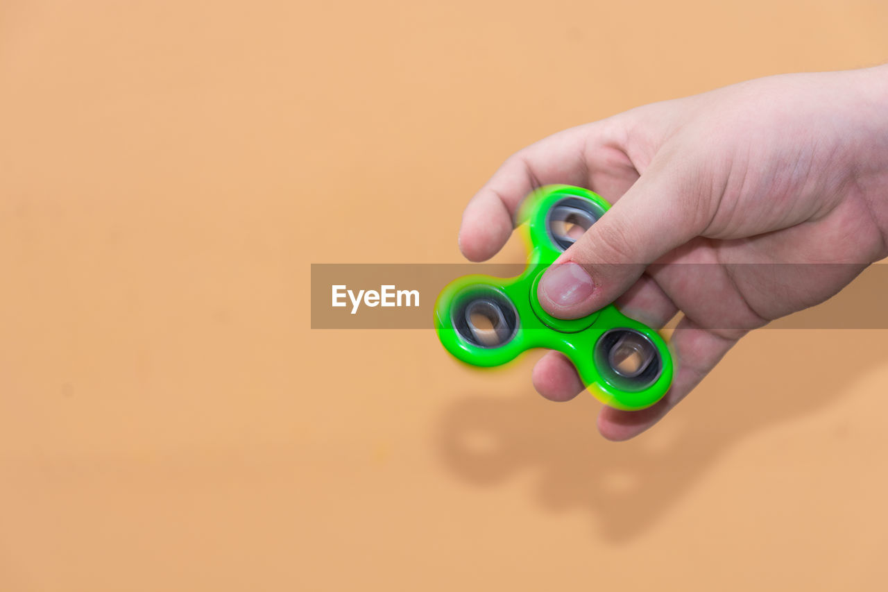 Cropped hand holding fidget spinner against brown background