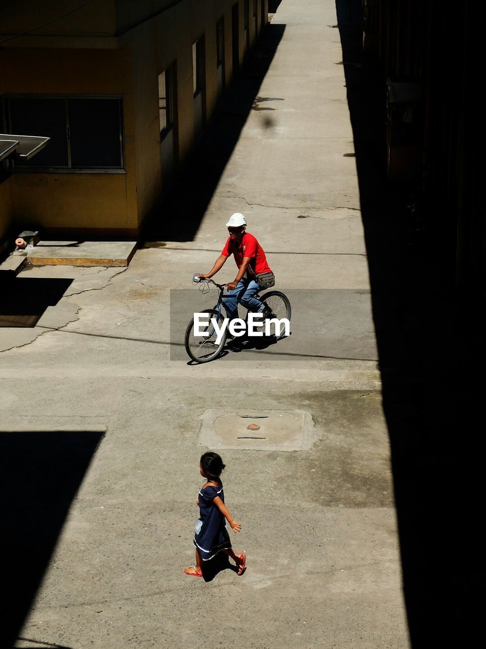 High angle view of man riding bicycle while girl walking on road in street