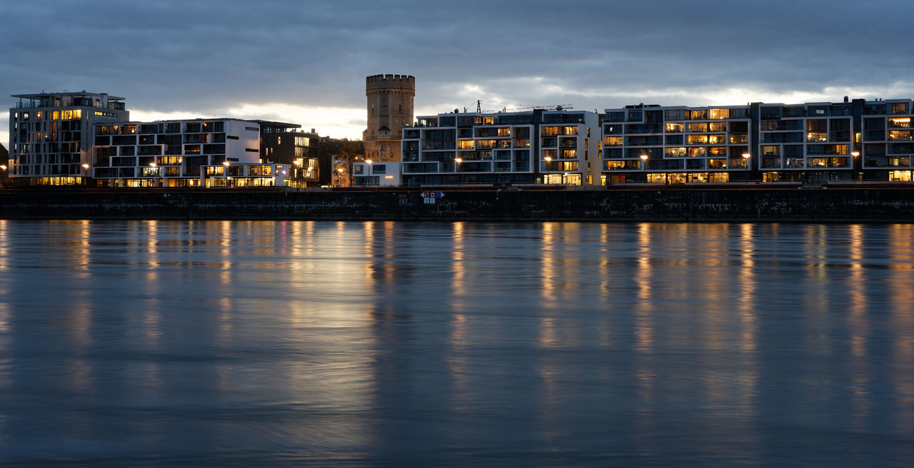 River rhine by illuminated buildings against sky at dusk in cologne