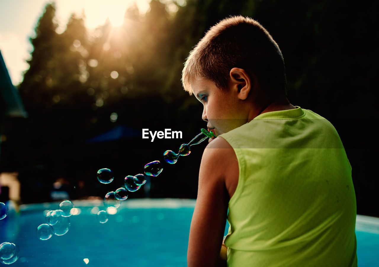 Rear view of boy blowing bubbles at poolside