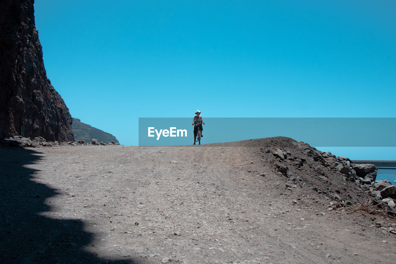 MAN STANDING ON SHORE AGAINST BLUE SKY
