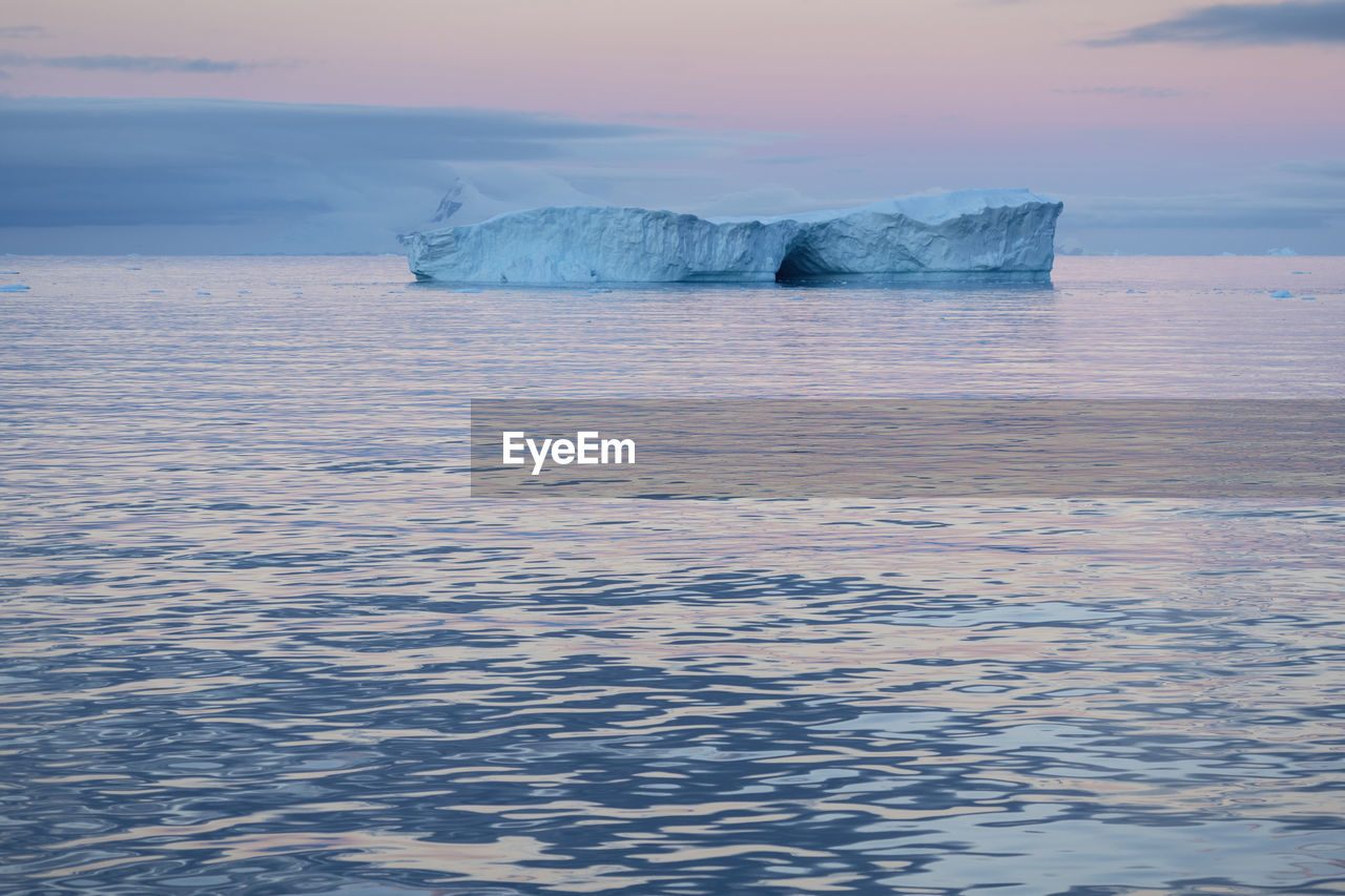 Scenic view of glacier in sea against sky during sunset