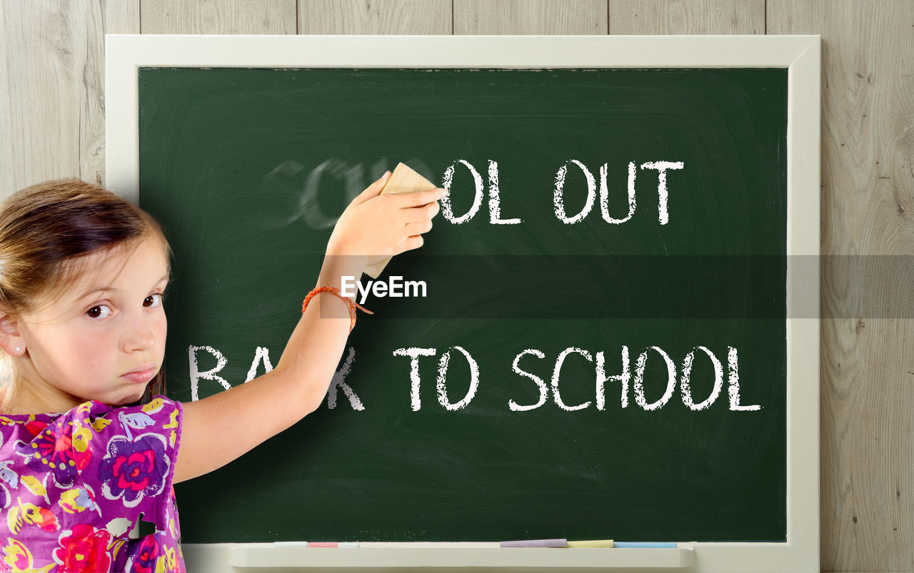 Portrait of girl erasing blackboard in classroom