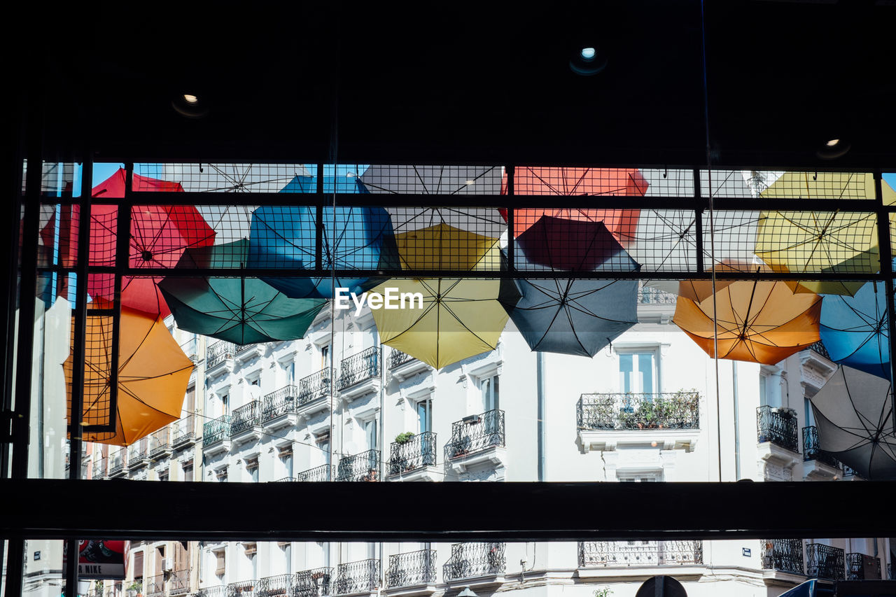 Low angle view of colorful umbrellas seen through window in city