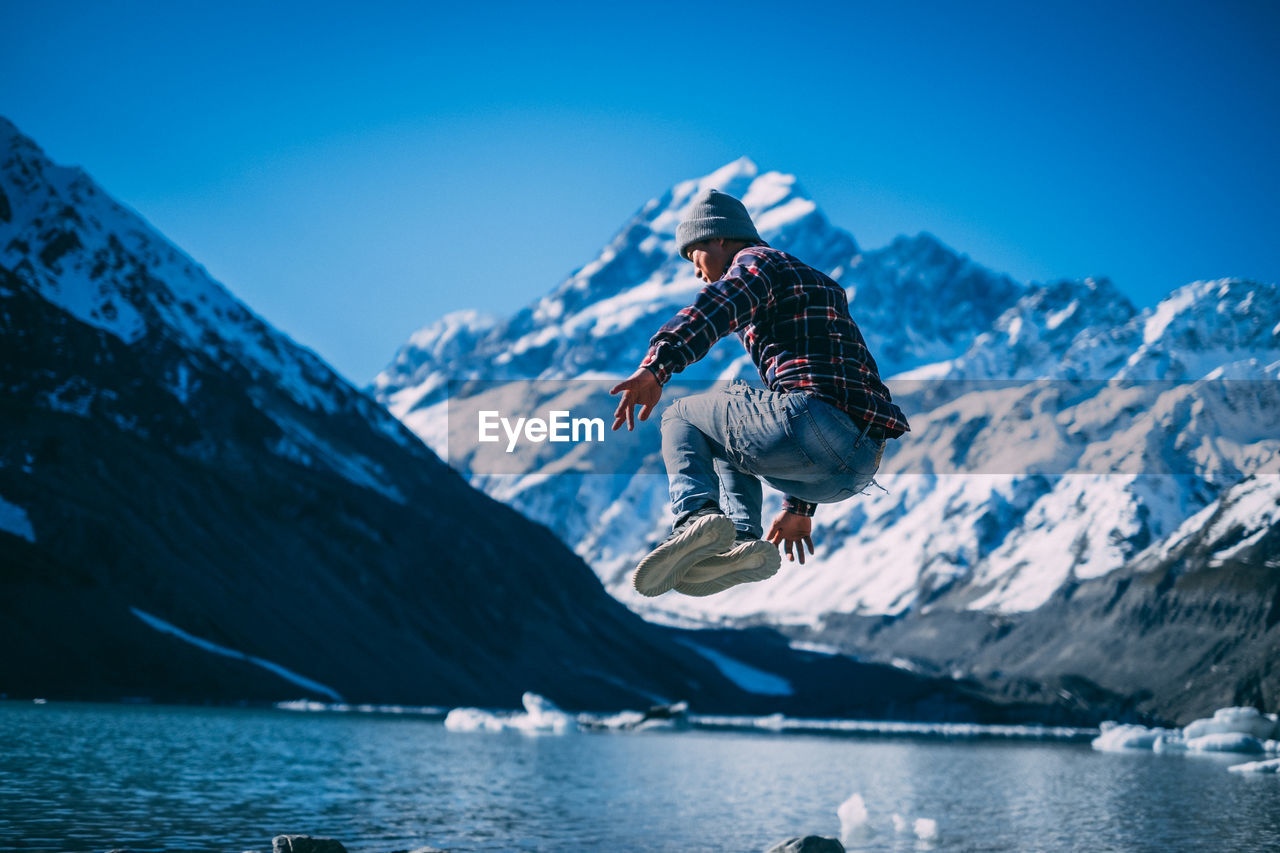Man jumping in mid-air by snowcapped mountains against sky