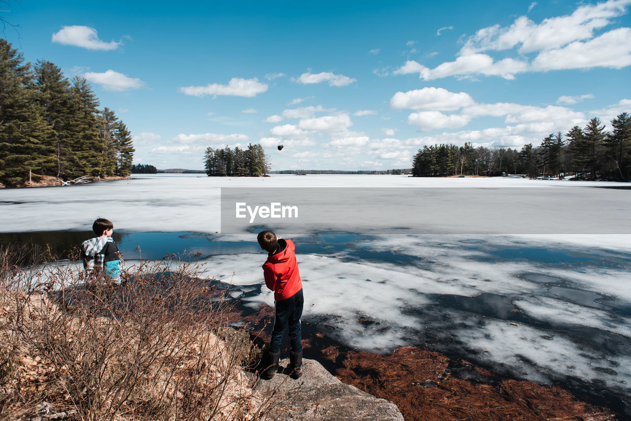 Two boys throwing rocks onto the ice on a lake on a spring day.