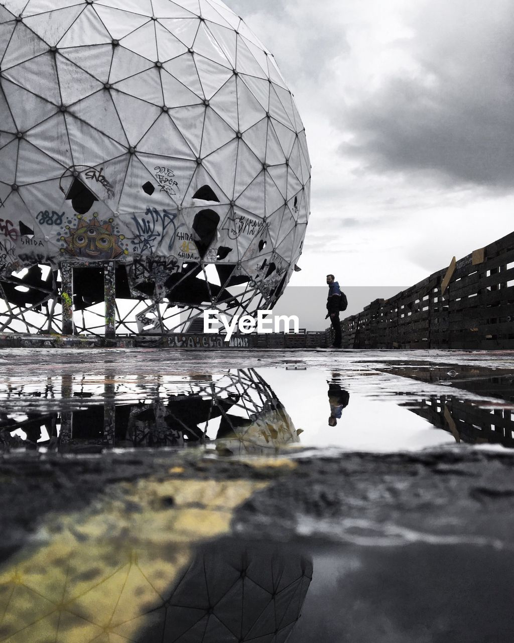 Man standing by abandoned dome on wet building terrace at teufelsberg during monsoon