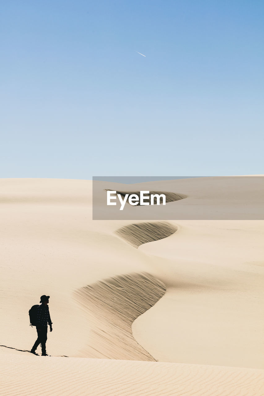 Man walking in desert against clear sky