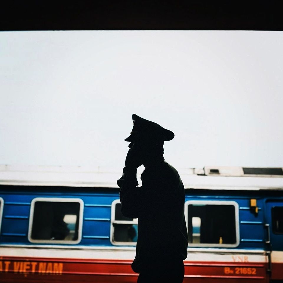 Silhouette transport conductor using phone with train in background