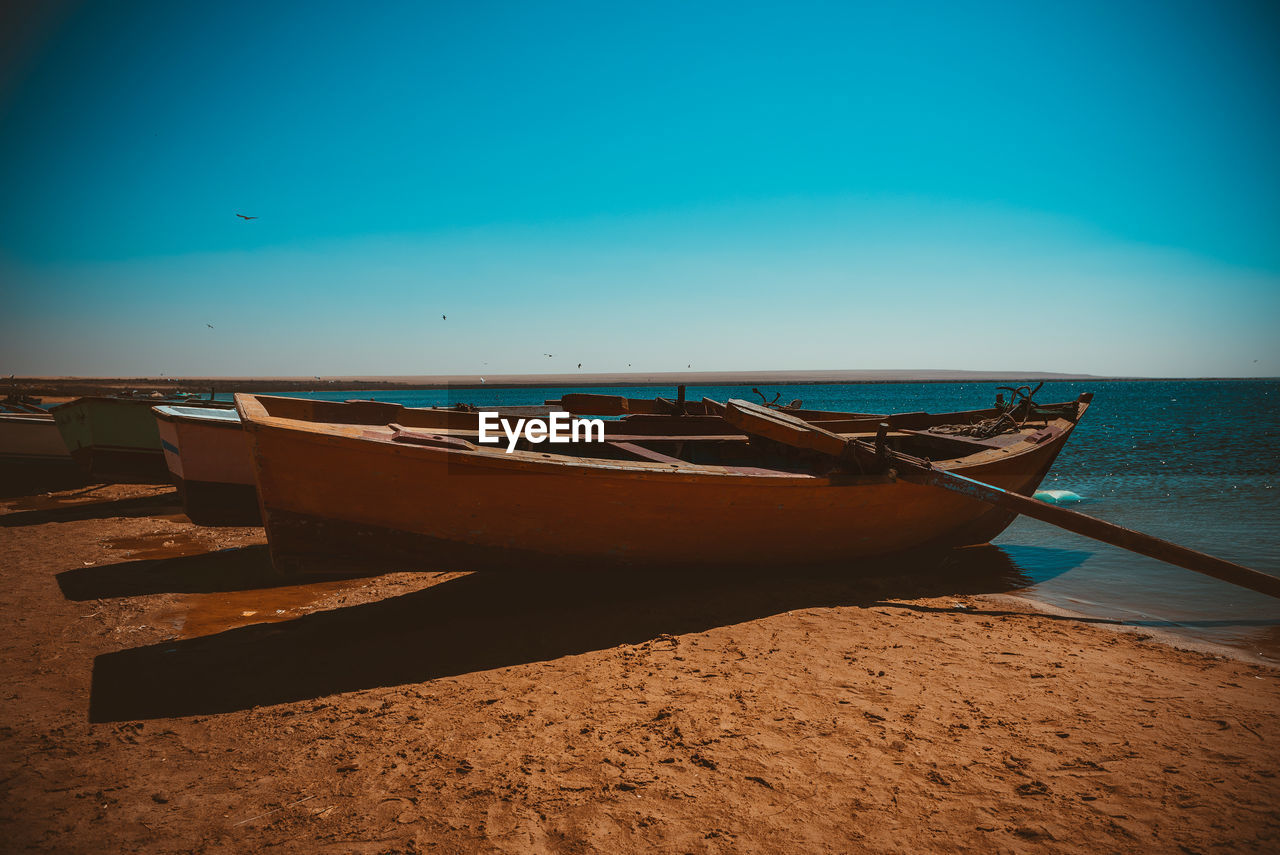 BOATS MOORED ON BEACH AGAINST CLEAR SKY