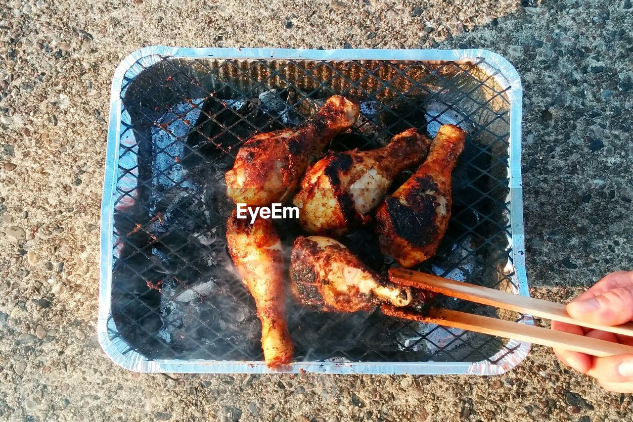 Cropped hand of person grilling meat on metal grate