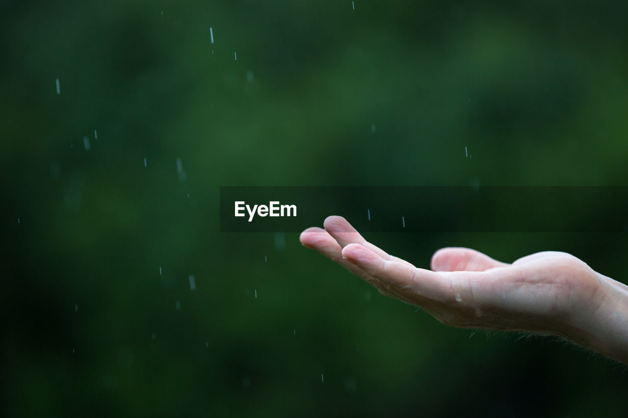 Cropped image of person with raindrops falling on hand