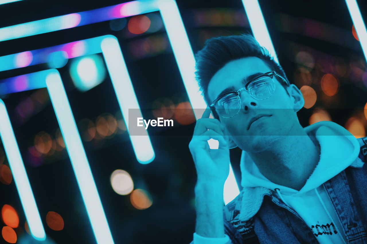 Close-up of thoughtful man wearing eyeglasses against lights at night