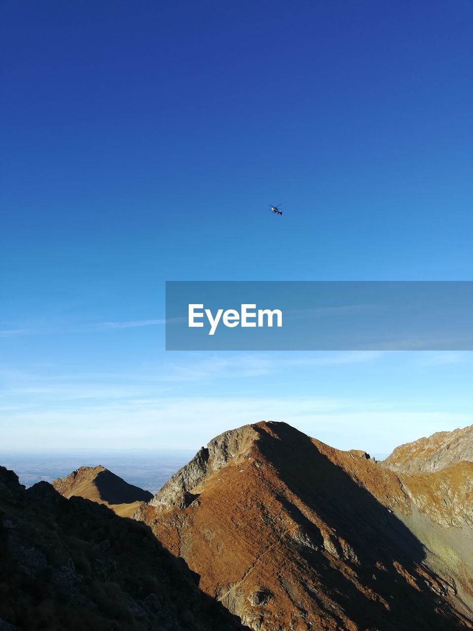 AIRPLANE FLYING ABOVE MOUNTAINS AGAINST BLUE SKY