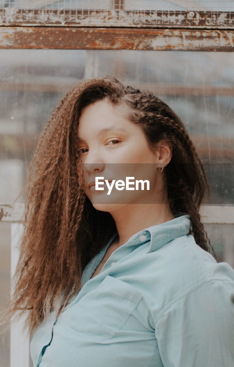 Portrait of beautiful young woman with curly hair standing against wall