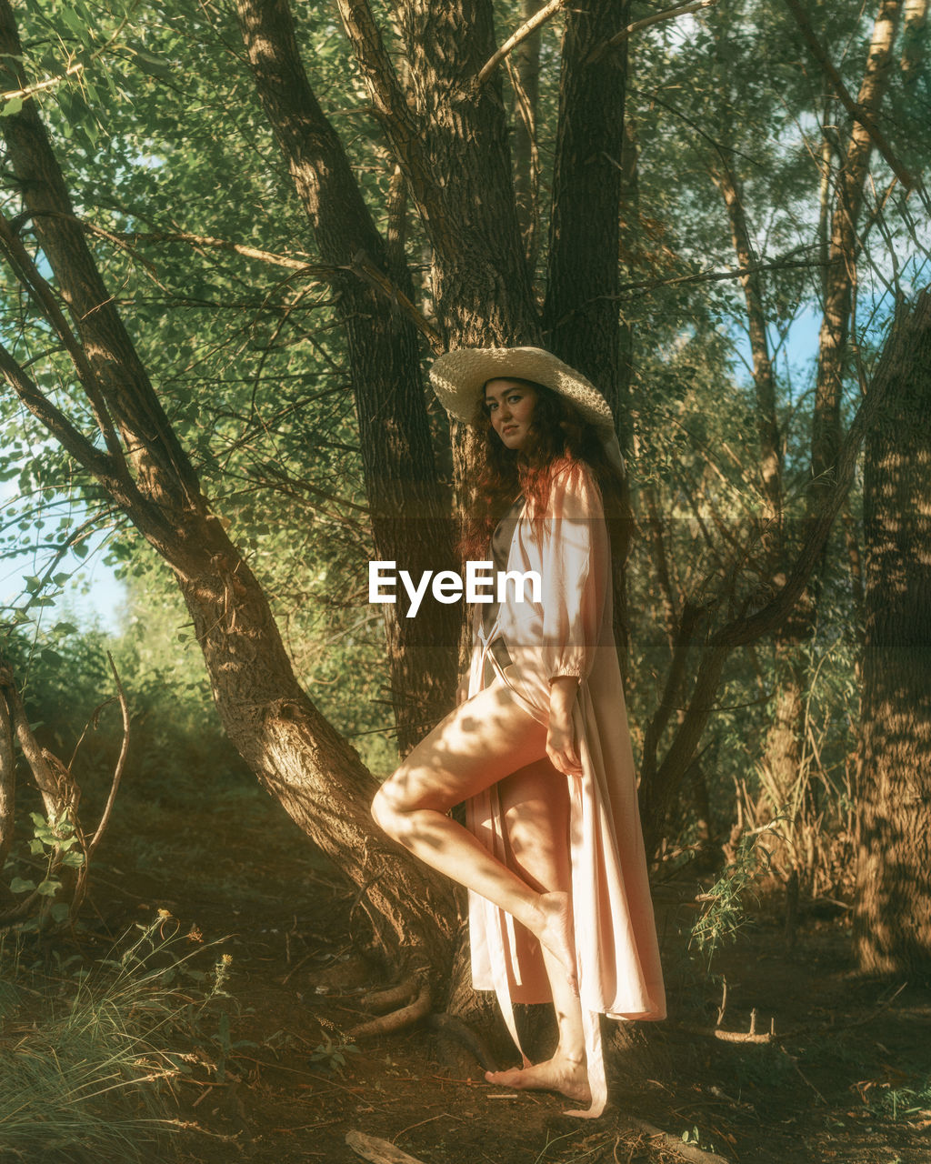 Woman standing by tree trunk in forest