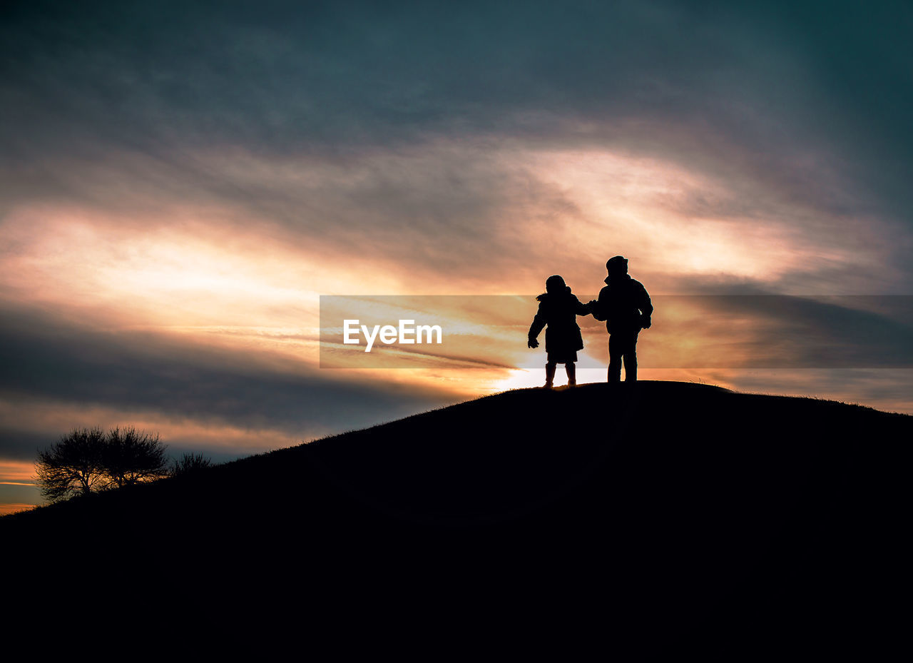 Silhouette children standing on hill against sky during sunset