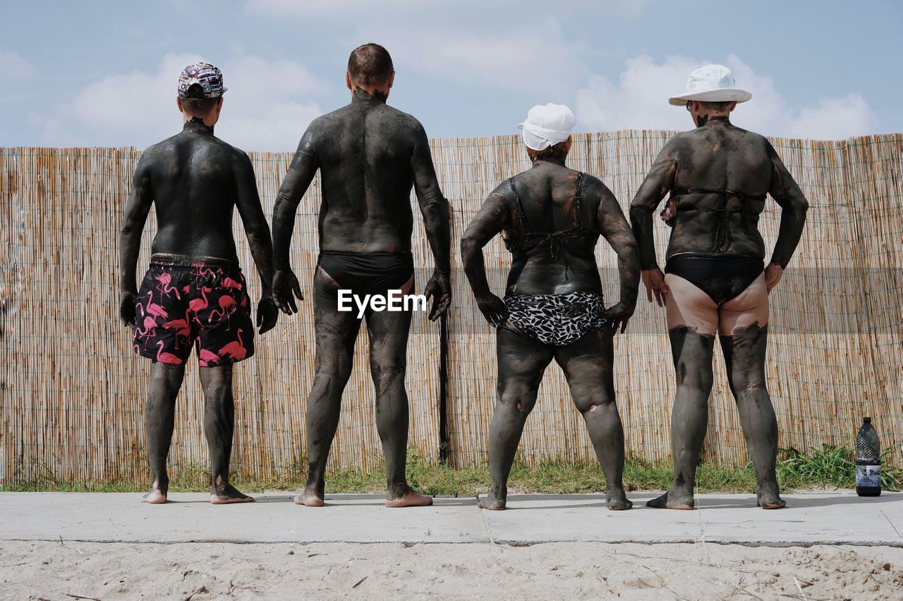 Rear view of friends covered in mud at beach