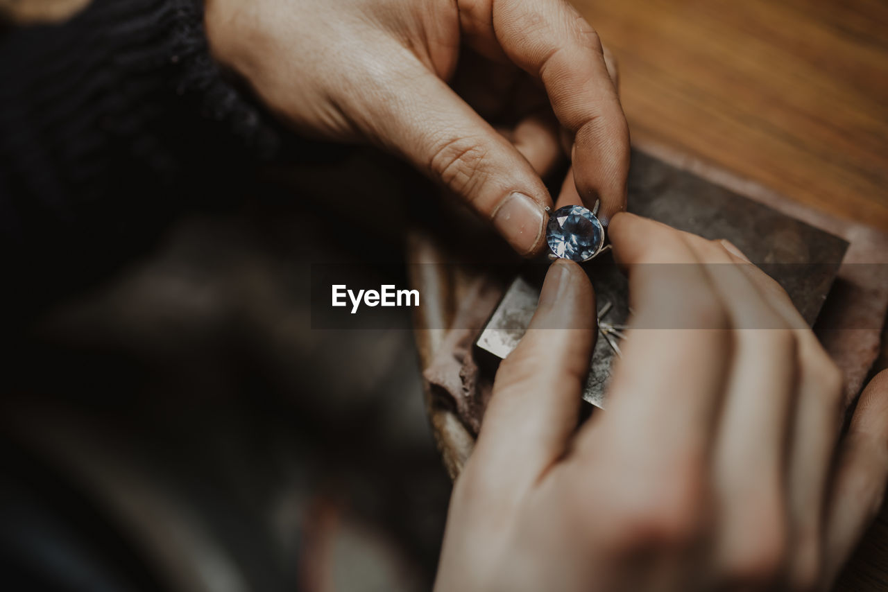 Unrecognizable goldsmith holding gem and metal ornament over table while making ring in workshop