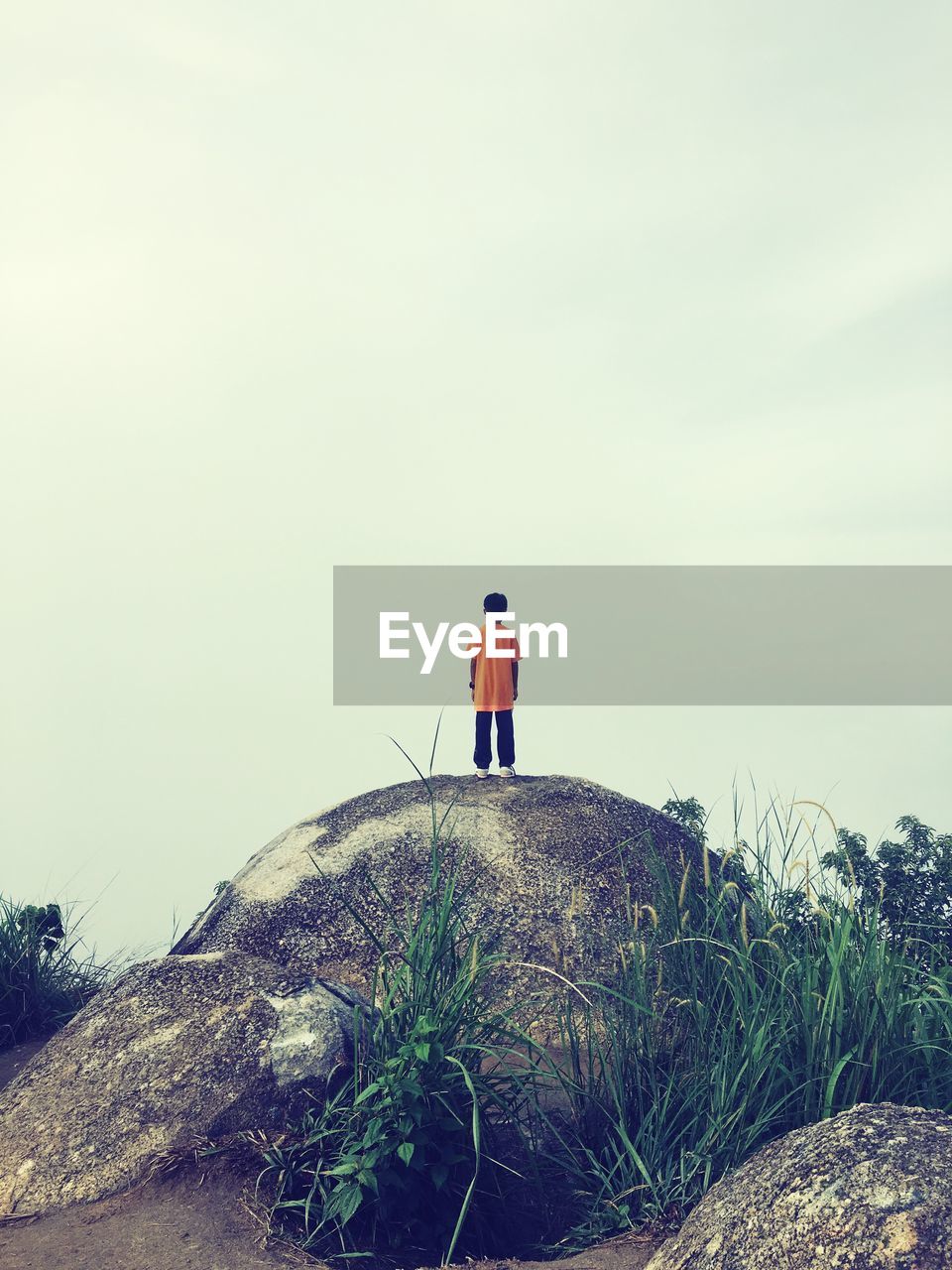 Rear view of boy standing on rock against sky