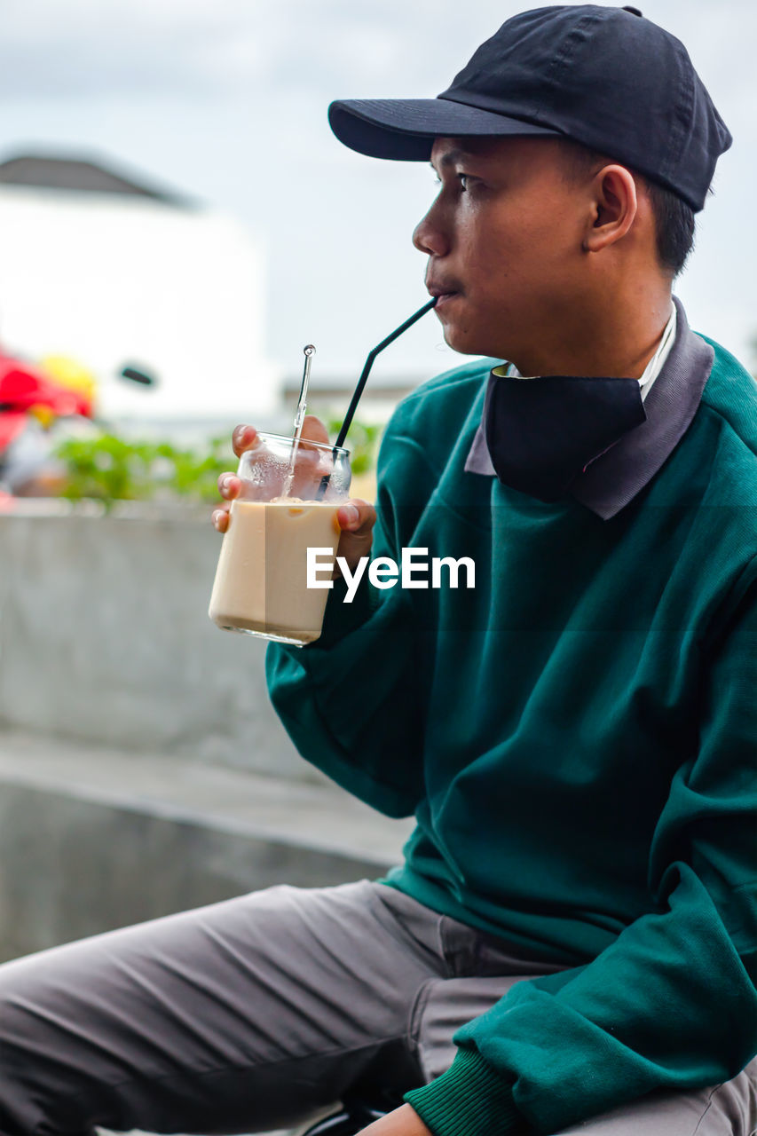 Man holding drink sitting in front of hat