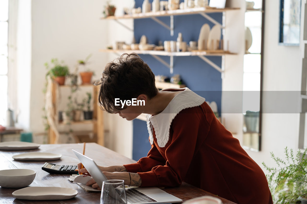 Focused artisan female pottery shop owner doing bookkeeping, measuring small business profitability